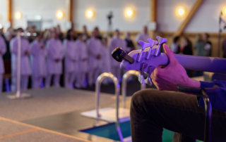 Gitarre mit Gitarrist von der Seite neben dem Taufbecken für Taufgottesdienst, im Hintergrund stehen Täuflinge