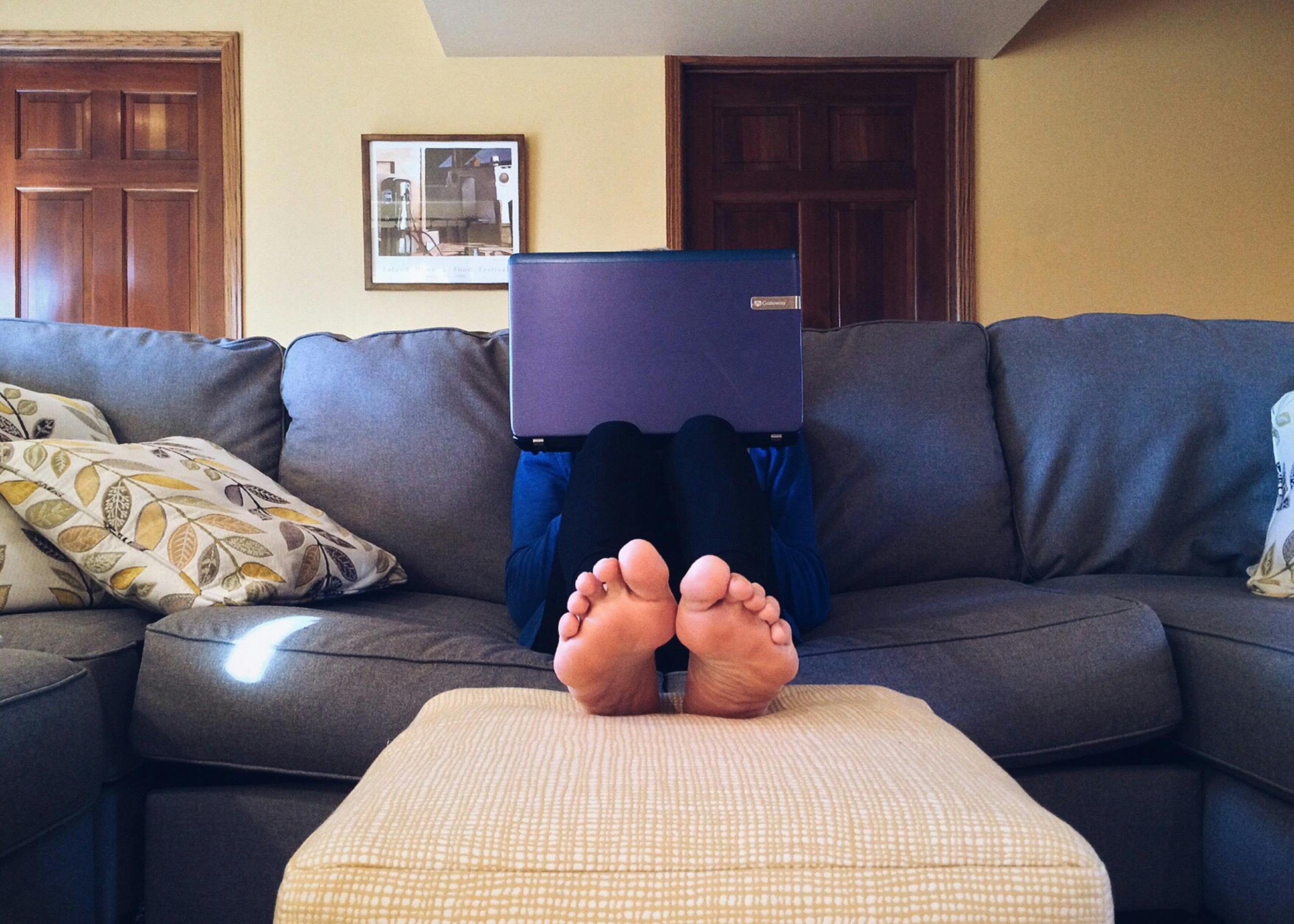 Mensch auf dem Sofa hinter dem Laptop im Vordergrund seine Füße
